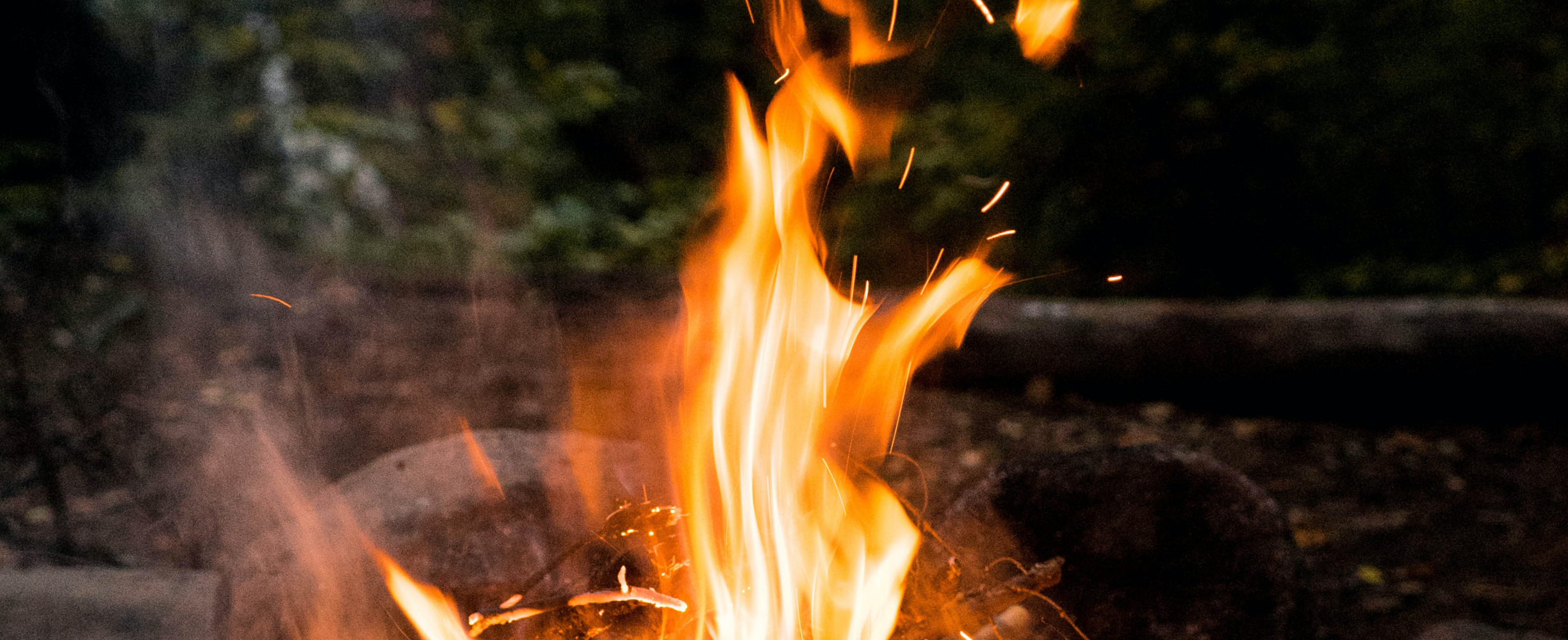 Oranssina roihuava nuotio kivien keskellä tummassa metsämaisemassa.