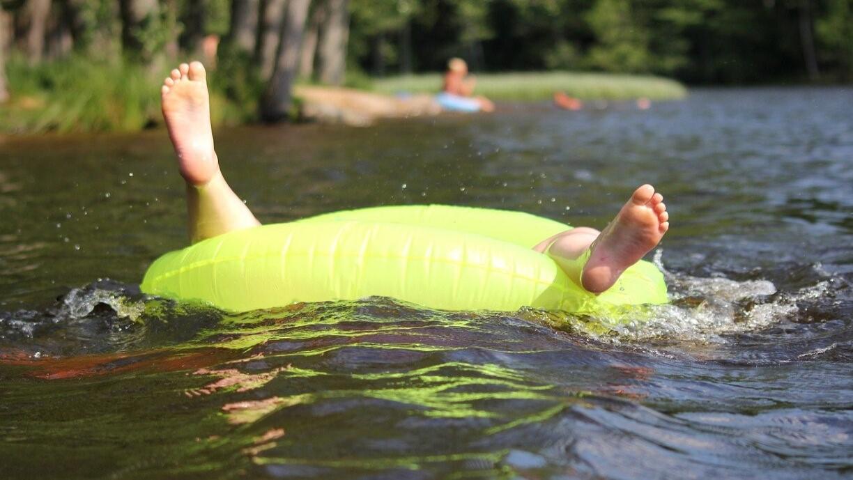 Lapsi leikkii järvessä uimalelulla siten, että vain hänen jalkansa näkyvät.