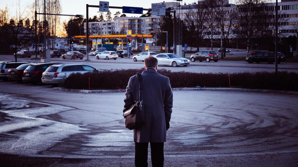 Mies seisoo kaupungissa ja katselee autotielle päin.