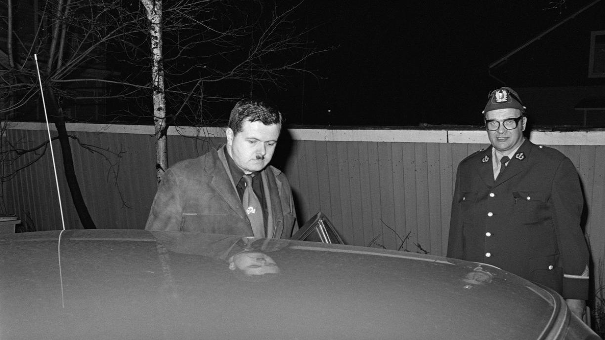 Mustavalkoinen kuva, jossa poliisi seisoo vieressä, kun Pekka Siitoin astuu autoon pidätettynä.