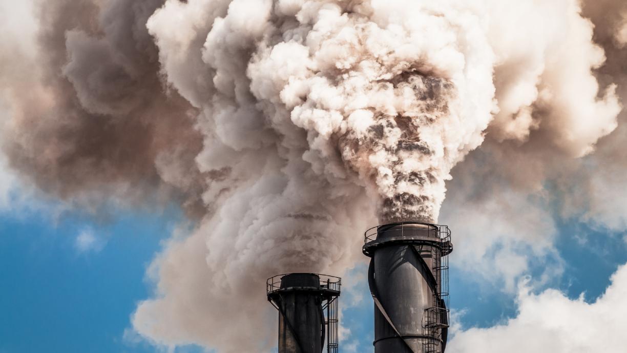 Kaksi tehtaanpiippua puskee taivalle vaaleanharmaata savua tai höyryä.