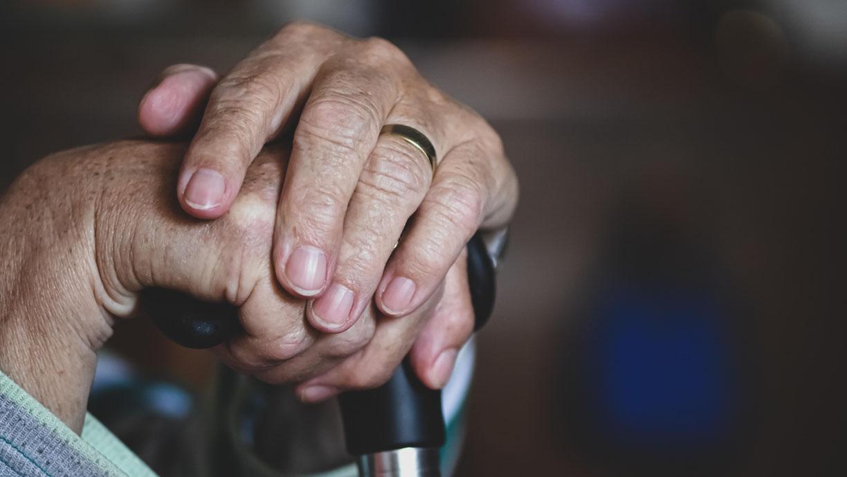 Vanhan ihmisen kädet nojaavat keppiin.