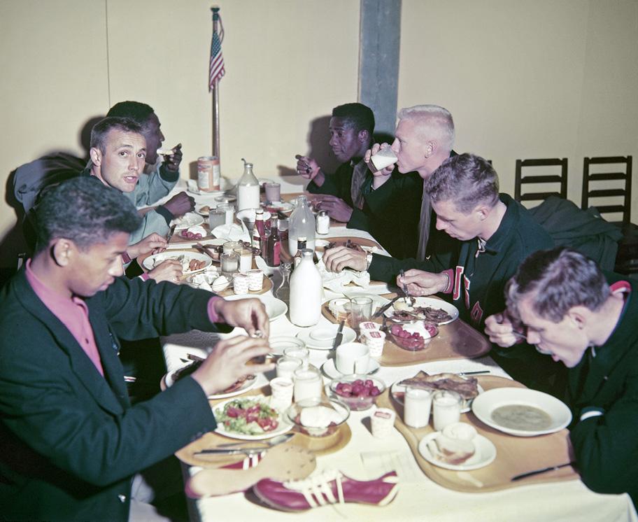 Seitsemän miestä istuu pöydän ääressä syömässä. Kullakin on oma tarjotin jolla on lautasia, laseja ja jälkiruokakulhoja. Lisäksi pöydässä on juoma- ja kastikepulloja. Pöydän etualalla tarjottimen vieressä on punaiset nahkaiset juoksukengät.