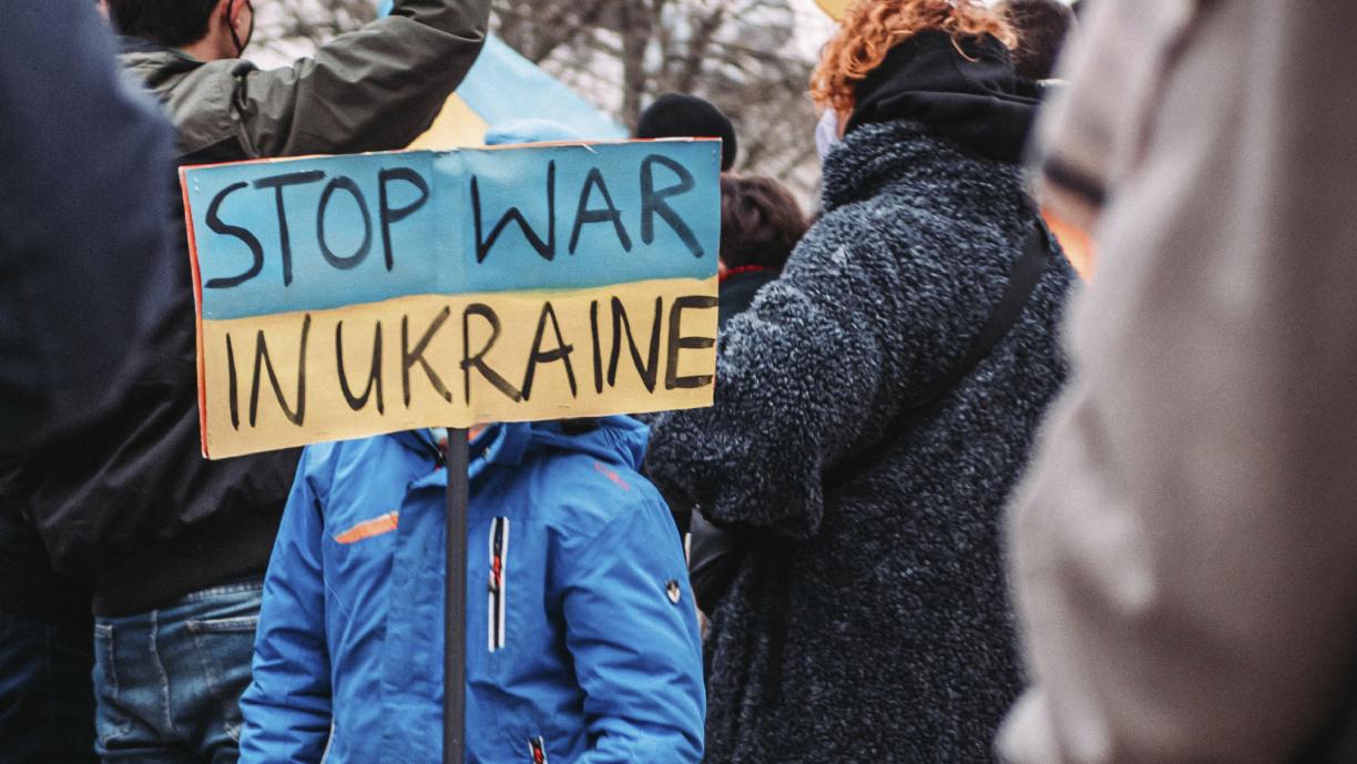 Ihmisiä mielenosoituksessa. Väkijoukon keskellä sinitakkinen henkilö pitää kylttiä, jossa lukee "Stop war in Ukraine".