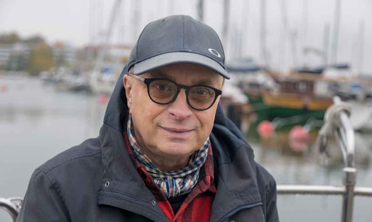 Mikko Huhtamies seisoo veneen kannella päässään lippalakki ja silmälasit.