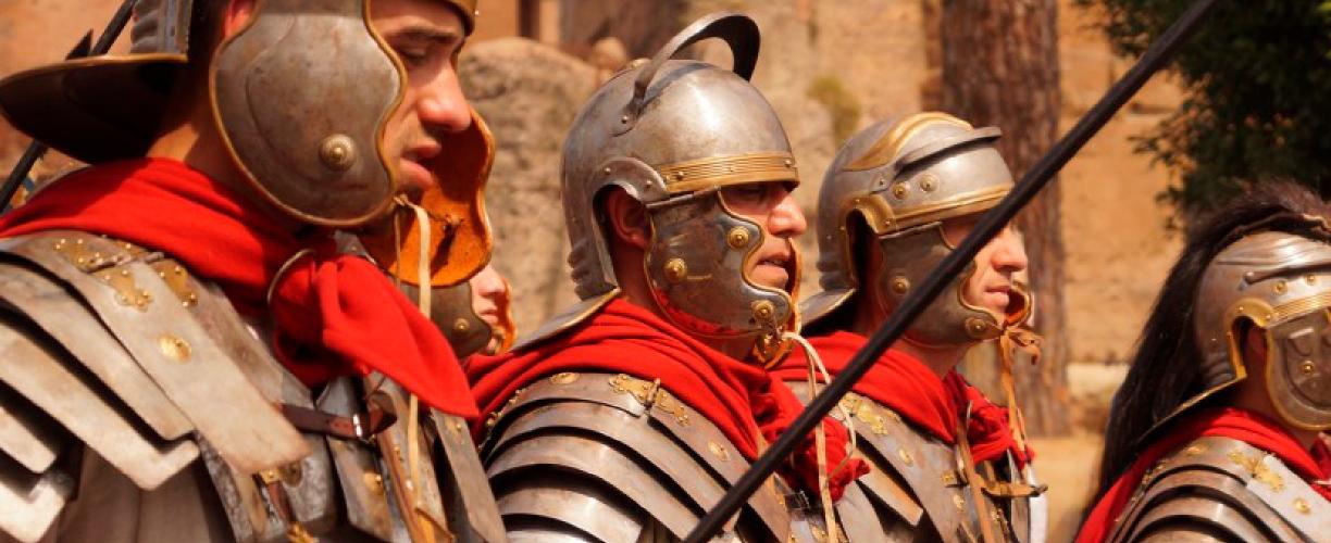 Kolme roomalaisiksi sotilaiksi pukeutunutta miestä marssii auringonpaisteessa. Heillä on päässään kypärät, käsissään jonkinlaiset keihäät ja kilvet ja yläruumiinsa suojana metallista ja nahasta valmistetut haarniskat.