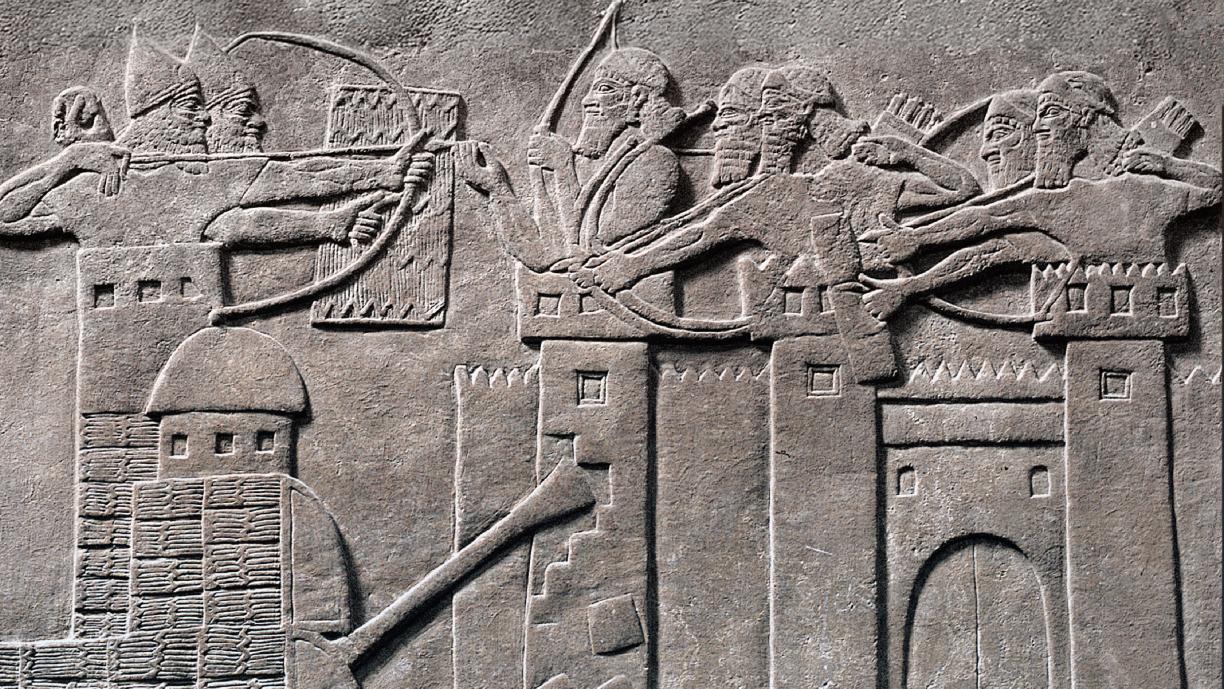 Kivireliefi, johon on hakattu tyylitelty kuva taistelusta. Jonkinlainen suuri liikuteltava hyökkäysvaunu murtaa suurta kaupunginmuuria. Sekä vaunun yläosassa että kaupunginmuurin päällä on sotilaita, jotka ampuvat toisiaan jousilla.