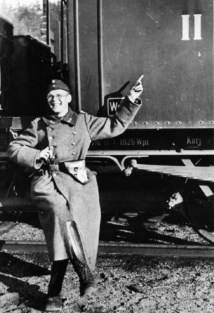 Mies istuu junanvaunun askelmalla pitkässä uniformun takissa.