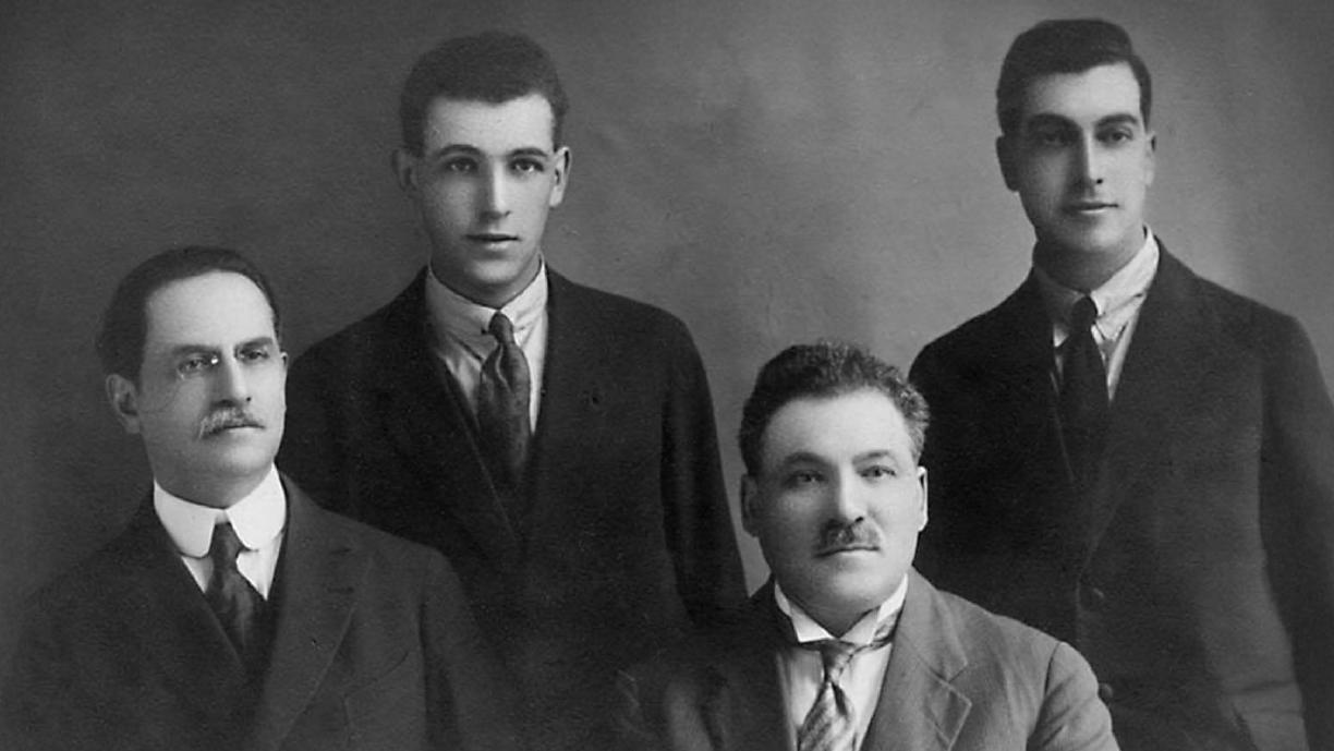 Mustavalkoinen valokuva, jossa on viisi miestä puvuissa ja kravateissa.