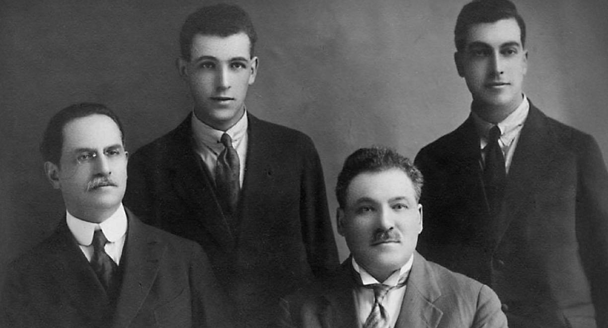 Mustavalkoinen valokuva, jossa on viisi miestä puvuissa ja kravateissa.