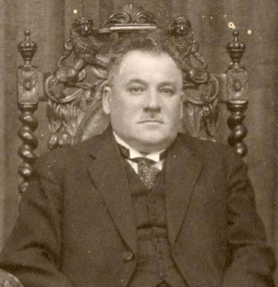 Mustavalkoinen valokuva, jossa mies istuu koristeellisesssa tuolissa.