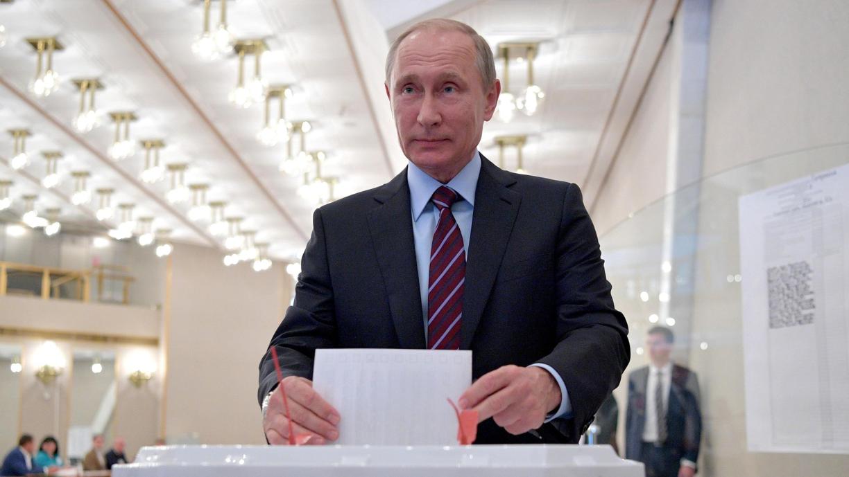 Pukuun ja solmioon pukeutunut mies asettamassa valkoista paperia suureen laatikkoon.