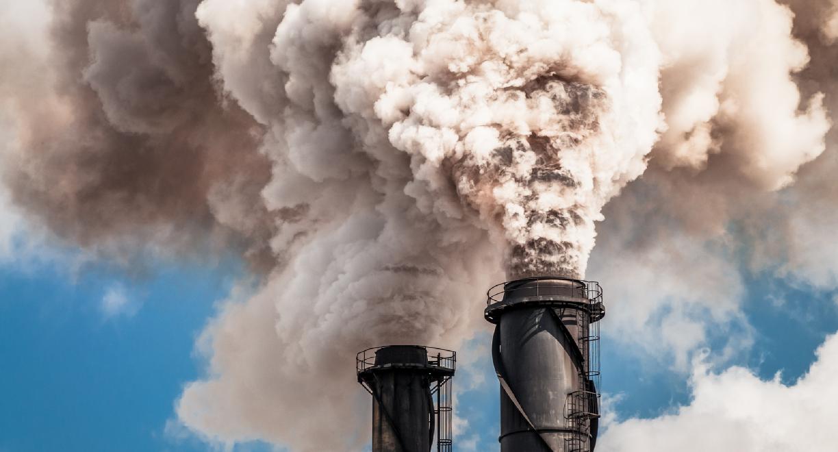 Kaksi tehtaanpiippua puskee taivalle vaaleanharmaata savua tai höyryä.