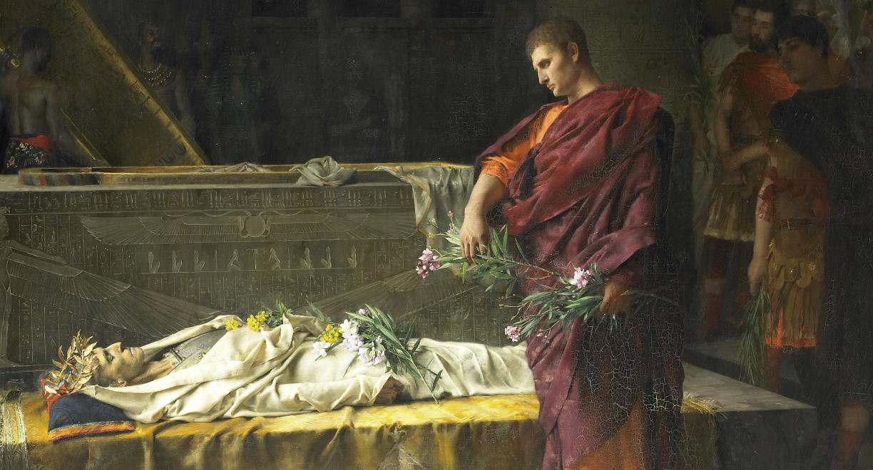 Öljyvärimaalaus, jossa punaiseen viittaan ja oranssiin vaatteeseen pukeutunut mies seisoo kivipaadella makaavan ruumiin äärellä kukkakimppu kädessään. Hänen takanaan näkyy jonossa muutamia muita miehiä. Ruumis on kääritty valkoisiin ja hänen päällään on kukkia.