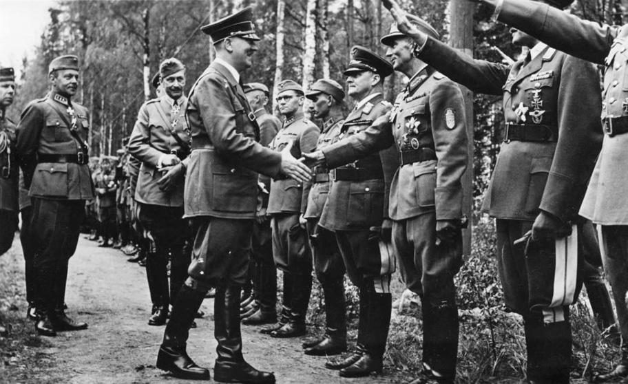 Mustavalkoinen kuva, jossa Hitler kättelee jonossa seisovia upseereita. Kalle Lehmus seisoo jonossa ja katsoo Hitleriin päin. Hitlerin takana kävelee Mannerheim.