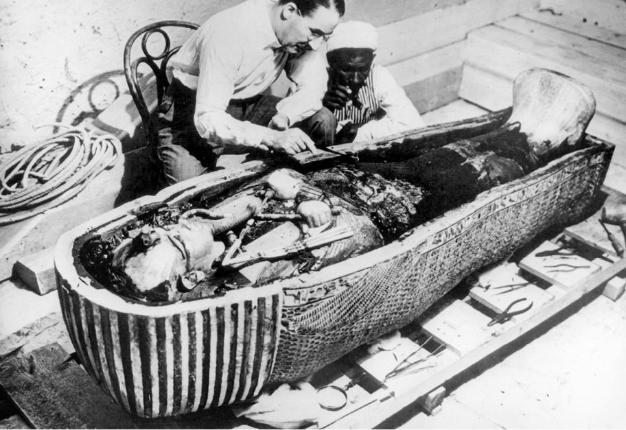 Mustavalkoinen valokuva miehestä, joka istuu avoimen sarkofagin äärellä tutkimassa siinä makaavaa muumiota.