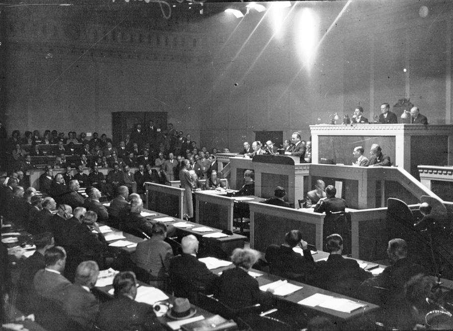 Mustavalkoinen valokuva suuresta salista, jossa istuu kymmeniä ihmisiä pitämässä kokousta.