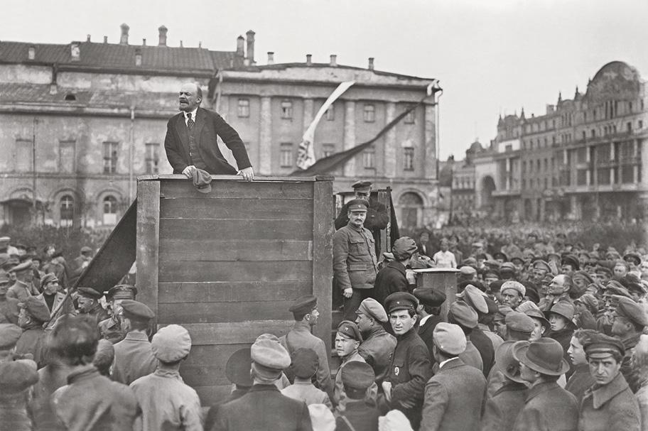 Mustavalkoinen valokuva, jossa suuri väkijoukko on kokoontunut kaupungin aukiolle. Keskellä on puinen koroke, jolla seisoo parrakas mies pitämässä puhetta.