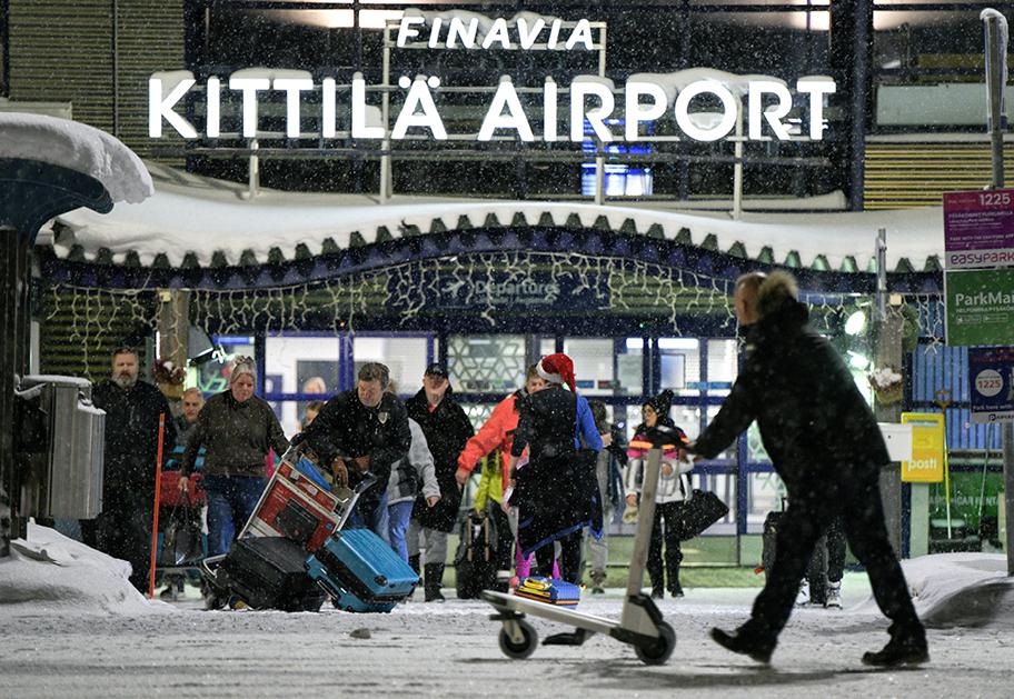 Kittilän lentoaseman edusta ulkoa kuvattuna. Ihmisiä lumisateessa tulossa ulos kentältä matkalaukkuja kantaen.