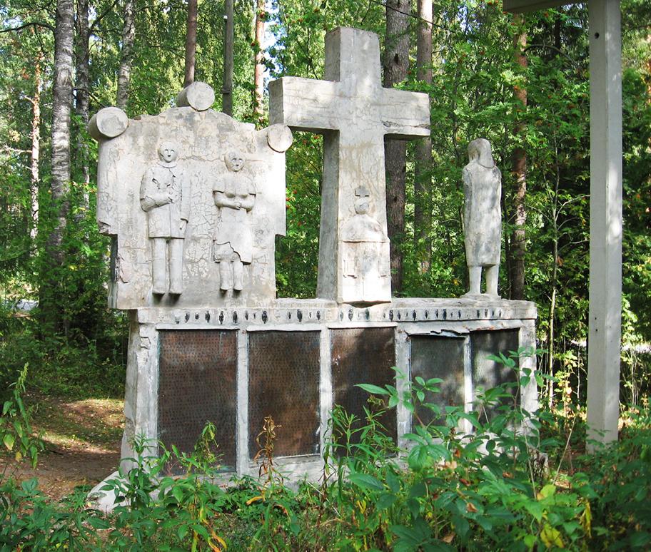 Suuri harmaanruskea patsas metsämaiseman keskellä. Patsaassa on keskellä suuri risti ja sen ympärillä kolme ihmishahmoa. Patsaan alaosassa on ruskeita laattoja joissa on tekstiä.