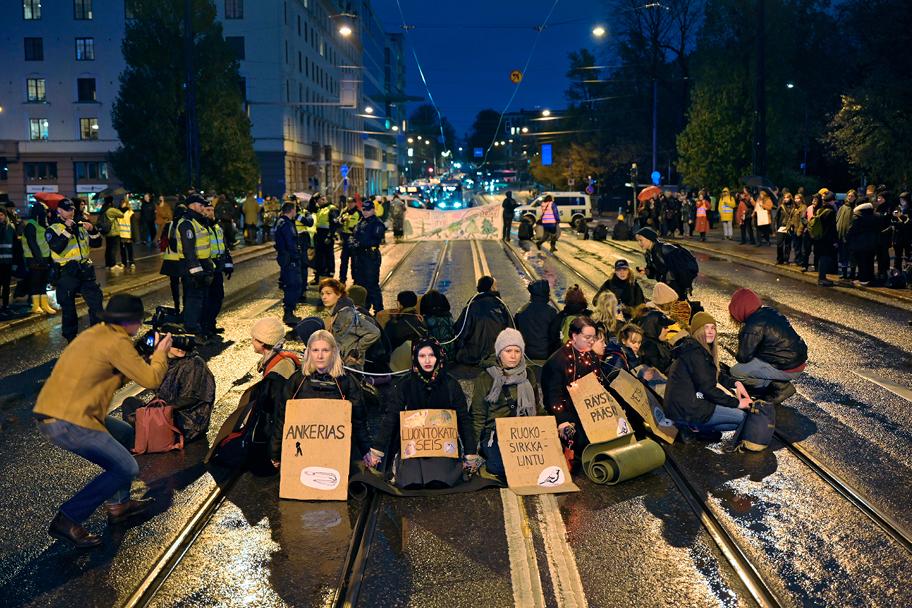 Ihmisjoukko istuu ratikkakiskojen päällä pimeässä kaupungissa ja pitelee mielenosoituskylttejä.