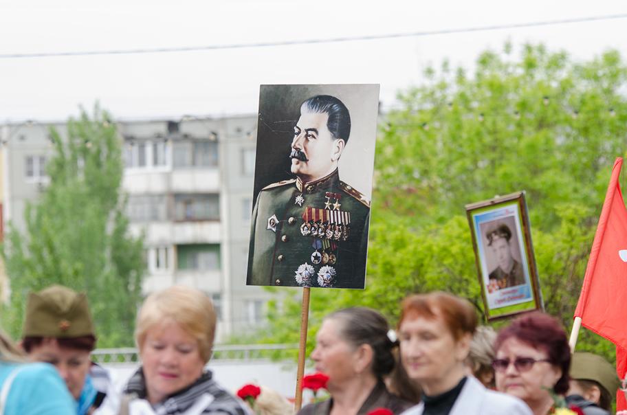 Väkijoukko kulkee ryhmänä kaupunkimaisemassa. Yksi heistä pitelee kookasta kuvaa Stalinista.