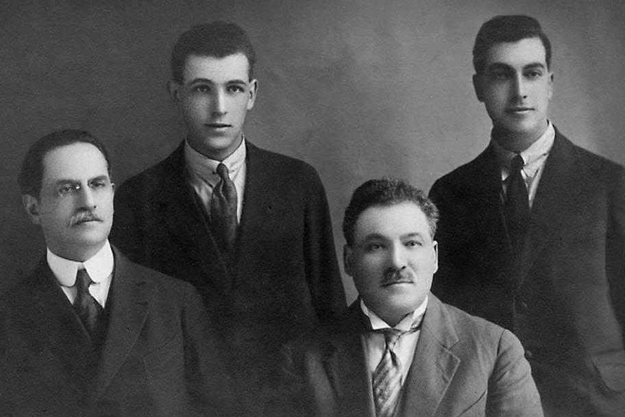 Mustavalkoinen valokuva, jossa on viisi miestä puvuissa ja kravateissa.