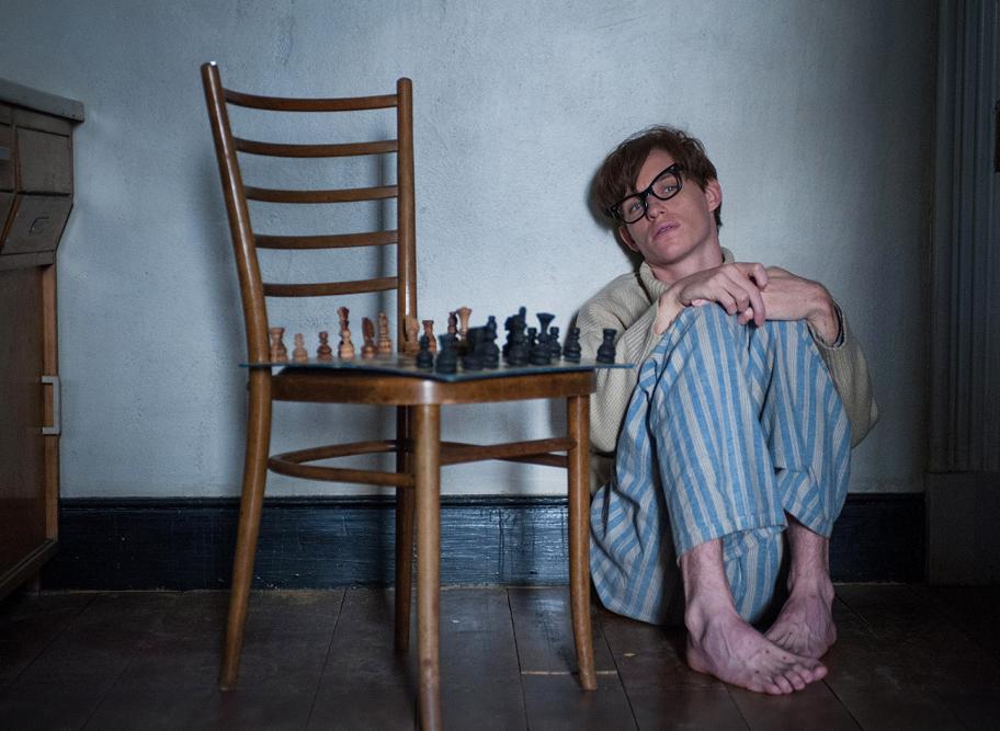 Nuori miesoletettu istuu seinän vieressä lattialla pyjamanhousuissa ja villapaidassa. Hänen vierellään on tuoli, jolla on shakkilauta.