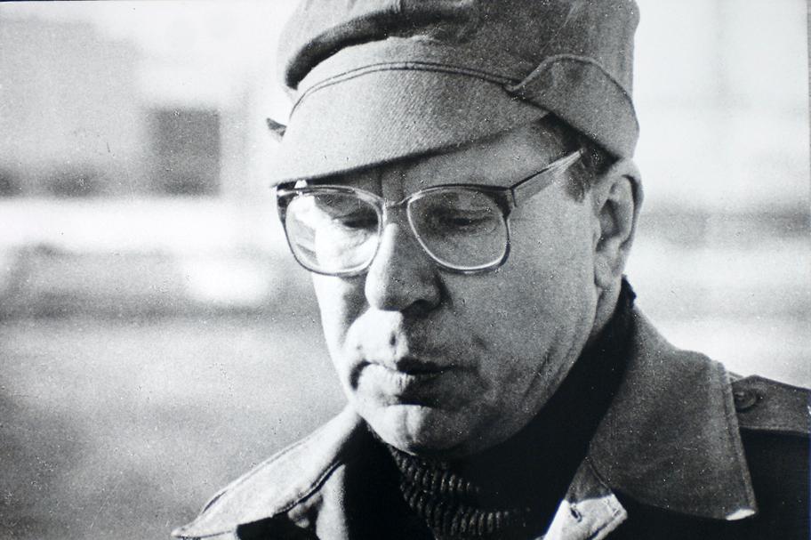 Mustavalkoinen valokuva, jossa on keski-ikäinen mies silmälaseissa, päässään lipallinen hattu ja yllään takki.